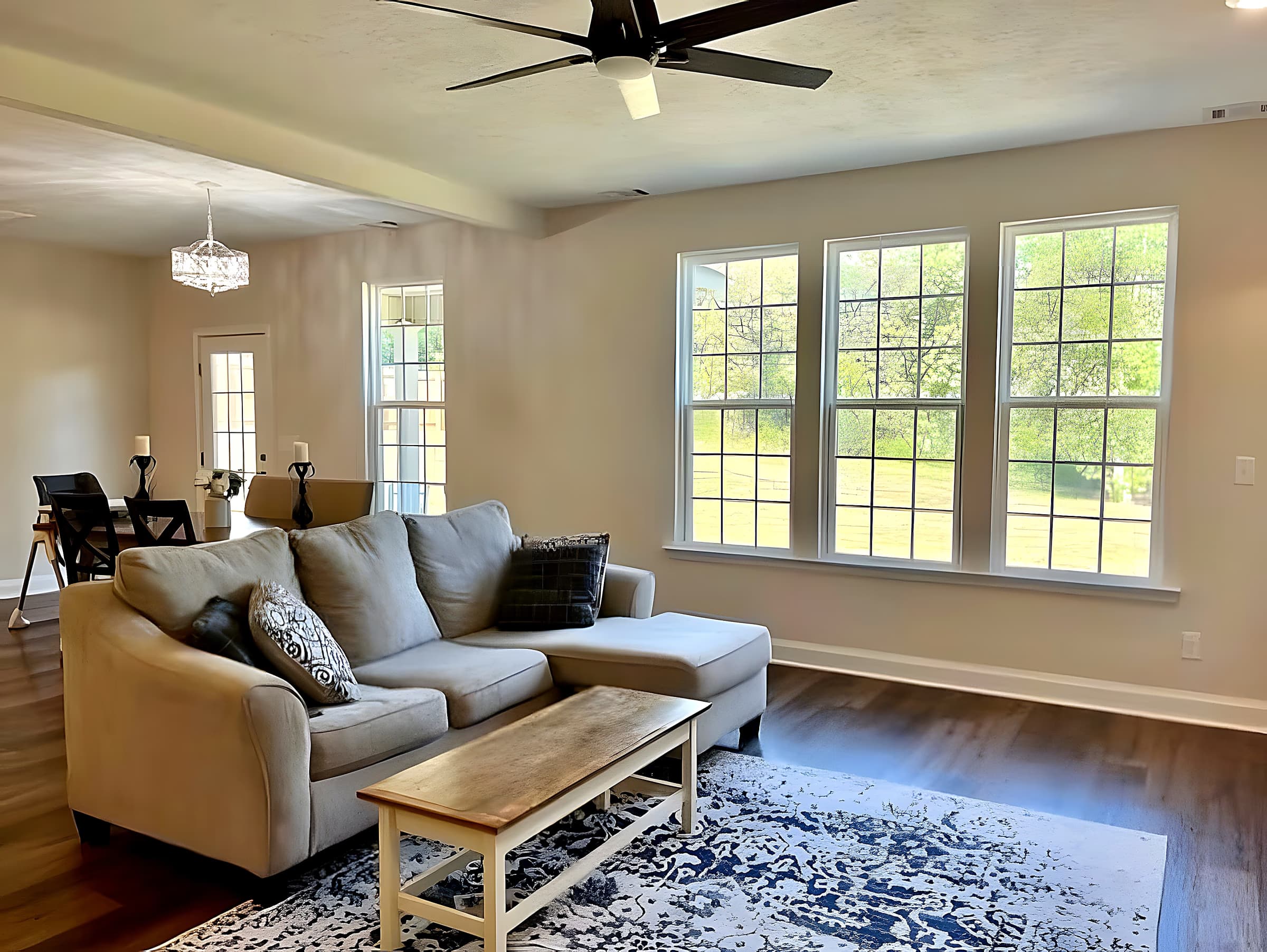 Living room with large windows, ceiling fan, and open flow to dining