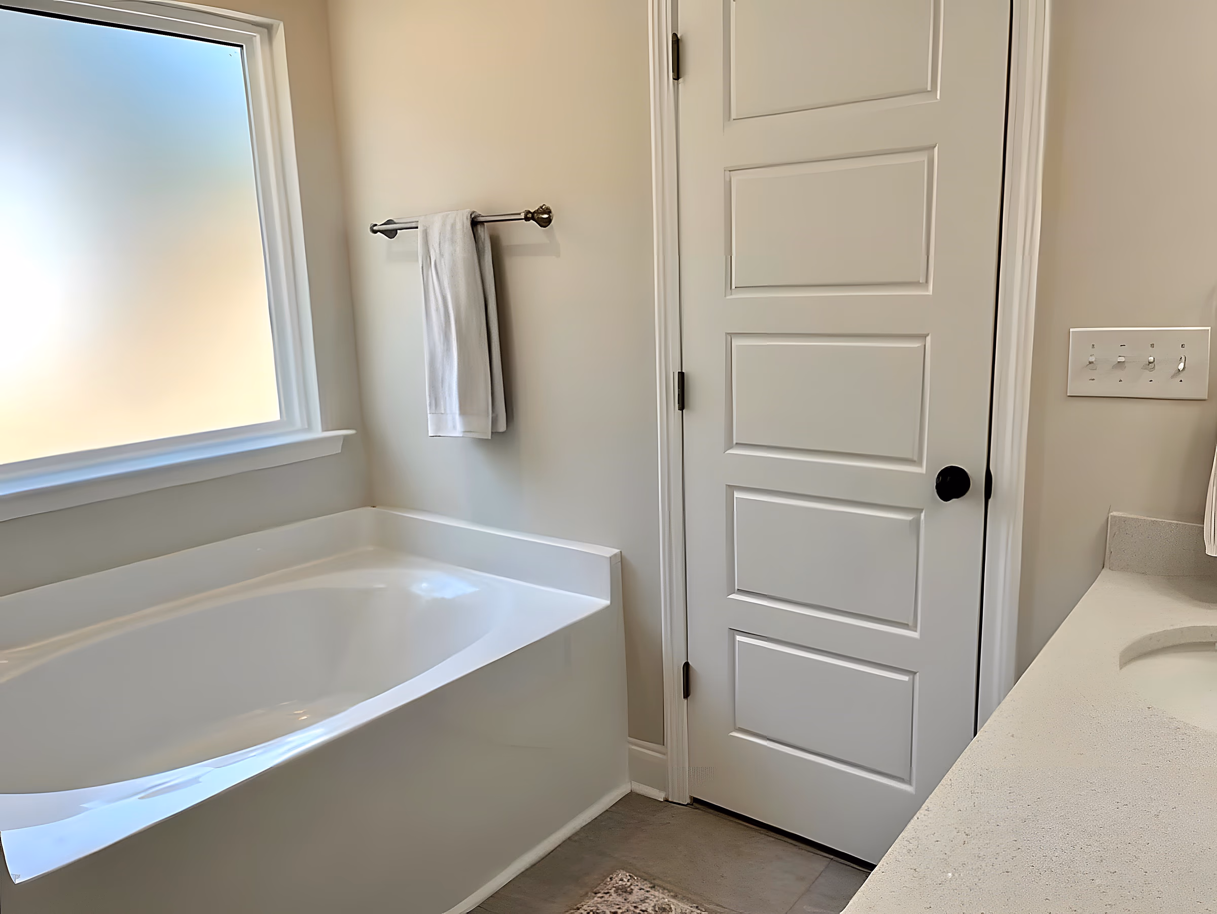 Primary bathroom soaking tub beneath a bright frosted window